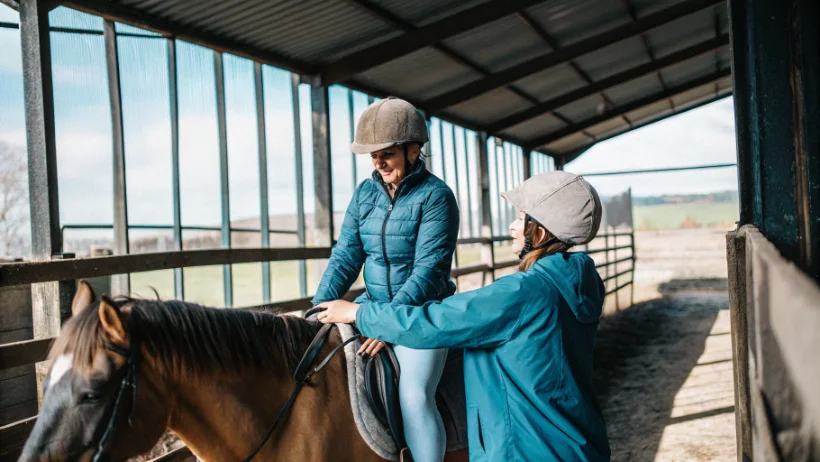 Riding instructor helping beginner mount horse at Cumbrian centre